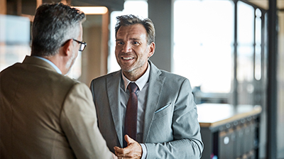 Two men wearing suits, speaking to each other wile in an office