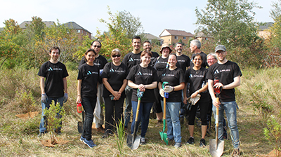 A group of people wearing an Applied Systems t-shirt and holding shovels while standing in a field 