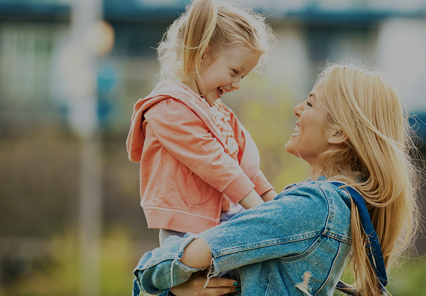 A woman holding her daughter in her arms, both are smiling and laughing. 