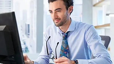 Man in business attire smiling while sitting at desk using a computer.