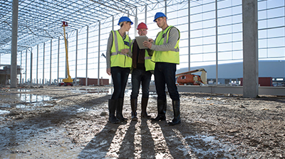 Three colleagues dressed in protective gear conversing at a construction site.