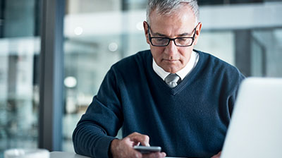 Man in business casual attire sitting and looking down at phone.