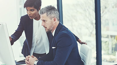 Two colleagues dressed in business attire looking at a computer screen.