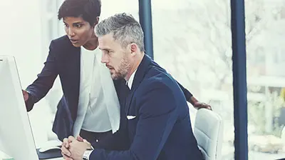 Two colleagues dressed in business attire looking at a computer screen.