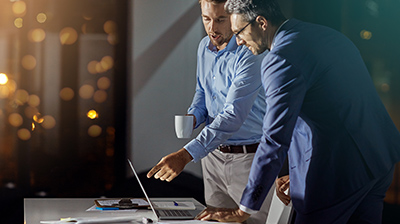 Two men dressed in business casual attire standing while interacting with a laptop.