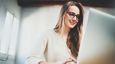 Woman in casual attire smiling while using a laptop.