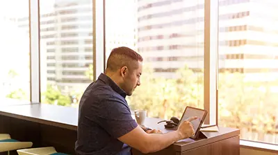 Man dressed in casual attire sitting at a table using a tablet.
