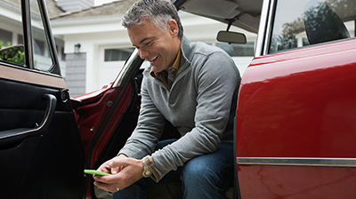 Man using cell phone while sitting on edge of car seat