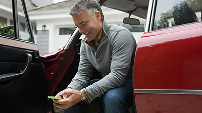 Man using cell phone while sitting on edge of car seat