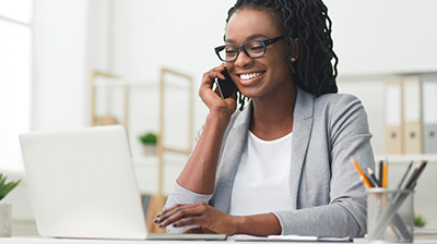 Businesswoman on phone call while using laptop at desk.