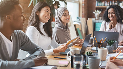 A group of coworkers having a meeting while sitting around a table with their laptops open 