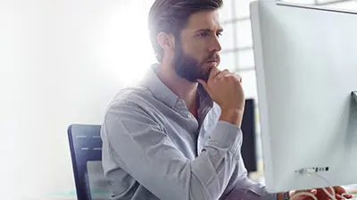 A man looking at his desktop monitor while his hand is holding his chin 