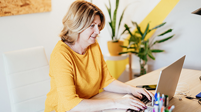 A woman in a yellow blouse typing on her laptop while sitting at a desk 