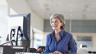 A woman dressed in business attire sitting at her desk while looking at a desktop monitor 