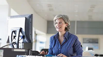 A woman dressed in business attire sitting at her desk while looking at a desktop monitor 