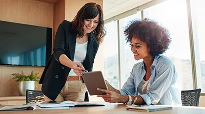 Two business women working on a project on a tablet in a bright conference room