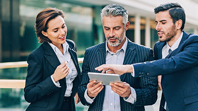 A woman and two men outside using a tablet