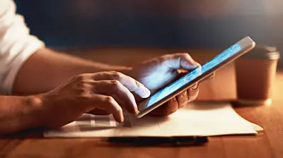 A man's hands resting on a table, holding a mobile phone
