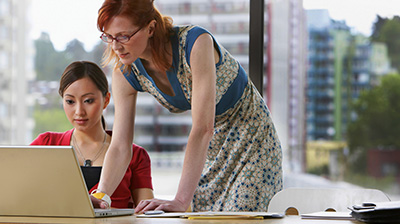 Two women working together on a laptop. One standing, one seated