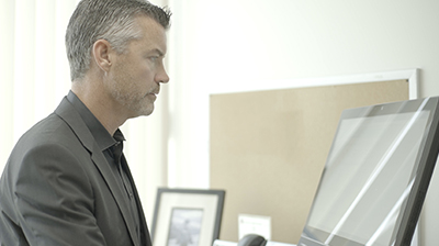 Man in business attire sitting in an office, he is looking down at a computer screen in front of him.