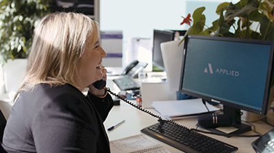 Woman dressed in business casual attire sitting at desk and smiling while holding phone.