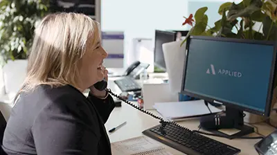 Woman dressed in business casual attire sitting at desk and smiling while holding phone.