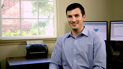 A man in a button-down shirt sitting in front of computers