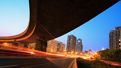 A time lapse under a bridge in a city with light trails from cars