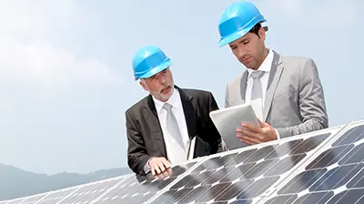 Two businessmen standing over solar panels reviewing items on a tablet
