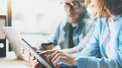 A man and a woman working on a tablet and a laptop
