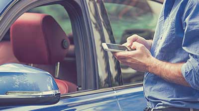 A man checking his phone next to his car