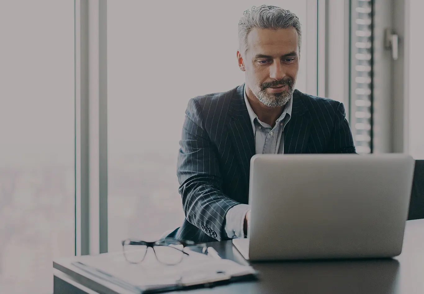 An aged business man in a suit is working on his laptop