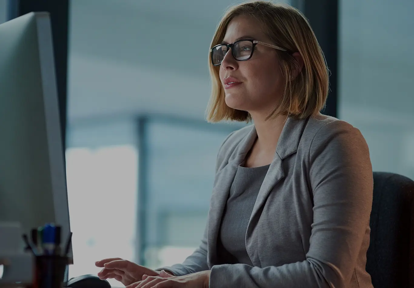 A business woman with blonde hair and glasses is working on a computer