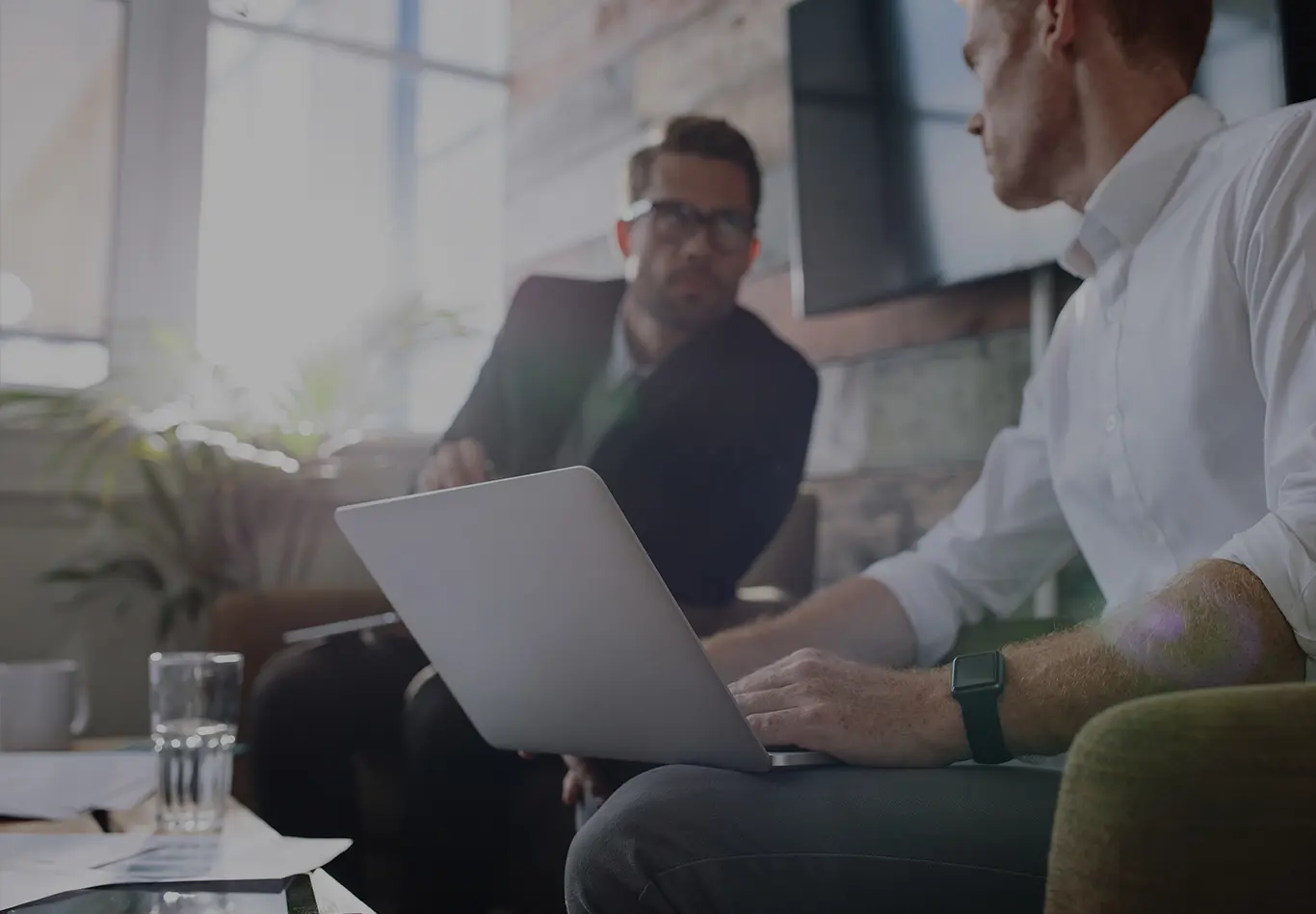 Two male business colleagues are talking to each other. One of the men has a laptop