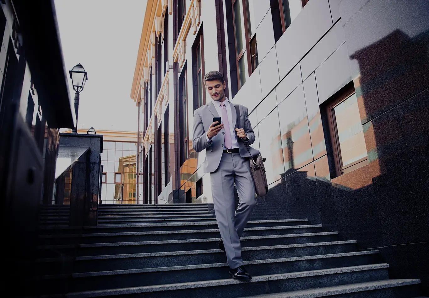 A man in a suit is walking down stairs and looking at a phone