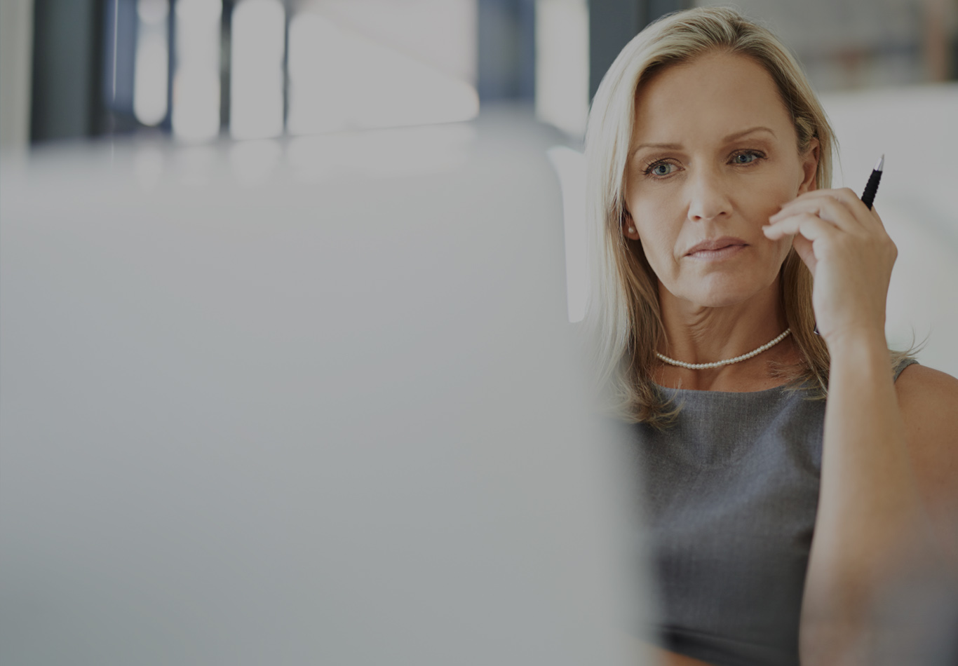 A blonde haired woman in business attire is looking a computer