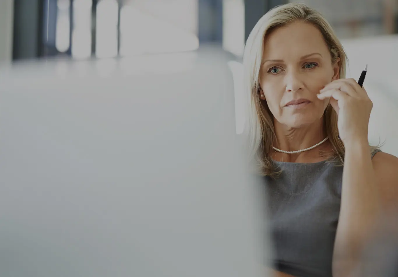 A blonde haired woman in business attire is looking a computer