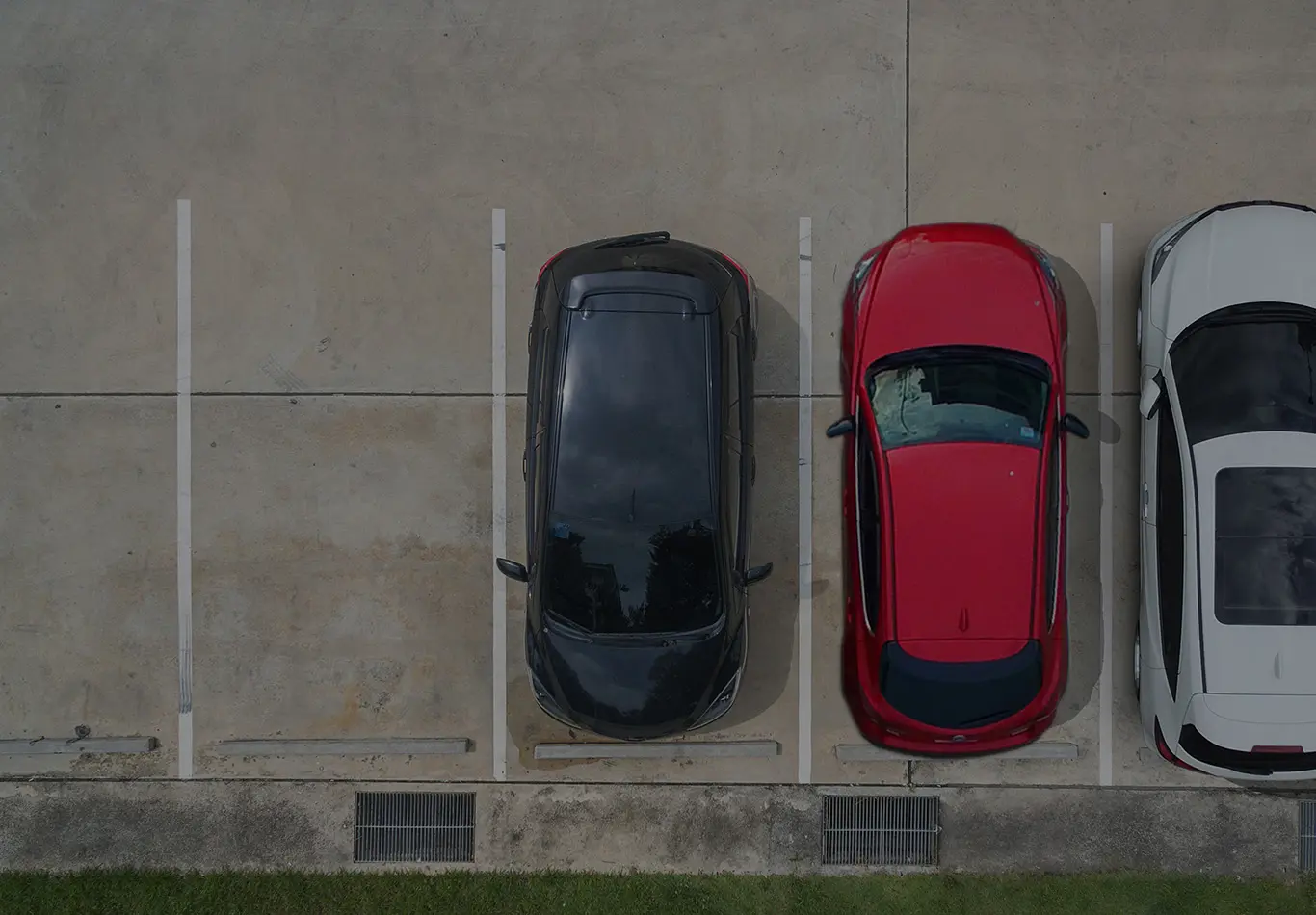 A white car, a red car, and a black car are parked next to each other in a parking lot