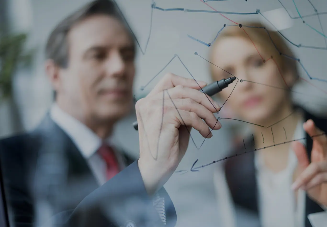 A man and a woman are out of focus and drawing on a glass board