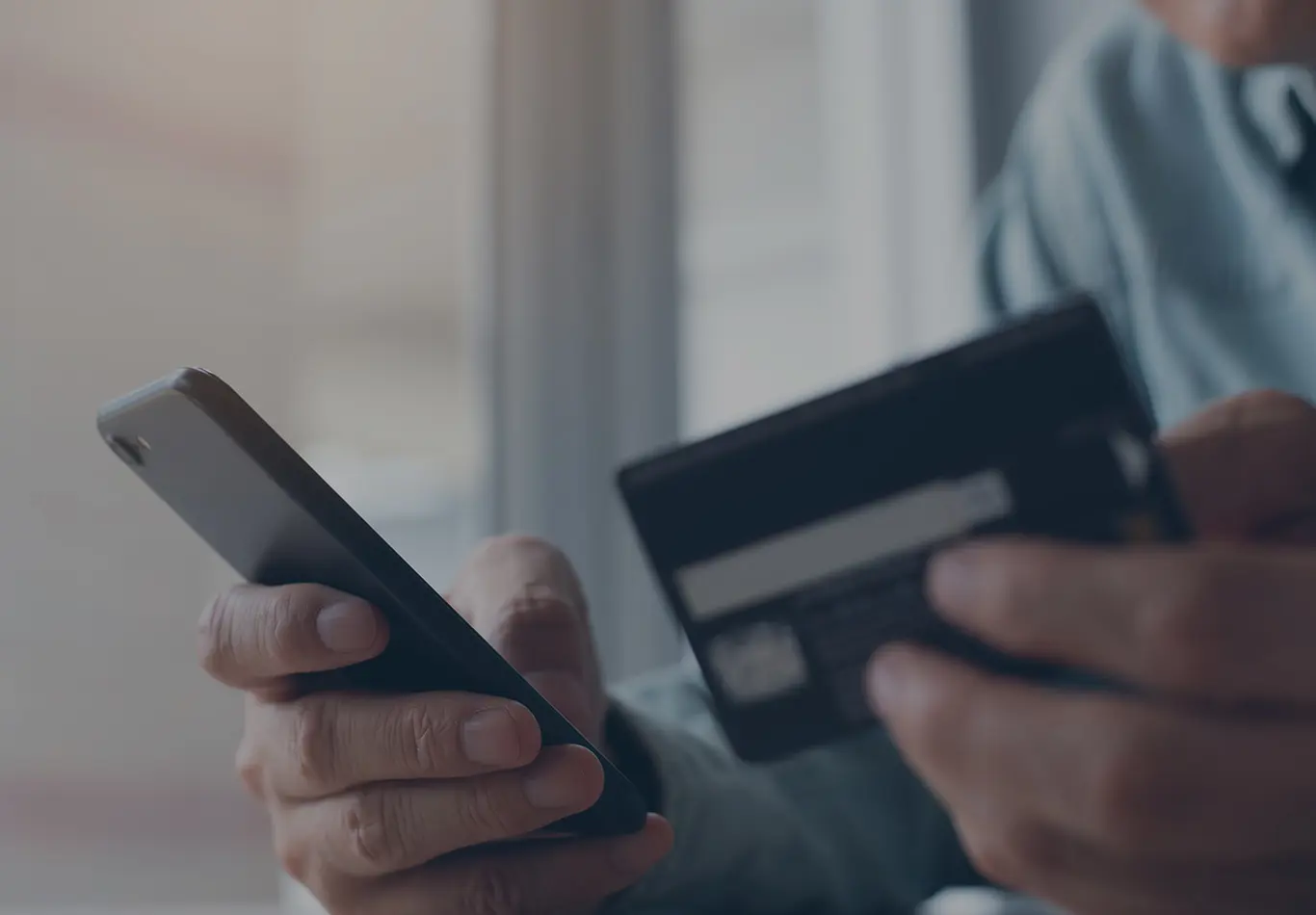 A person is holding a phone in one hand and a credit card in another
