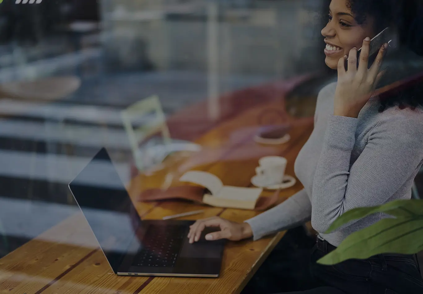 A smiling woman is talking on her phone with her laptop in front of her. 