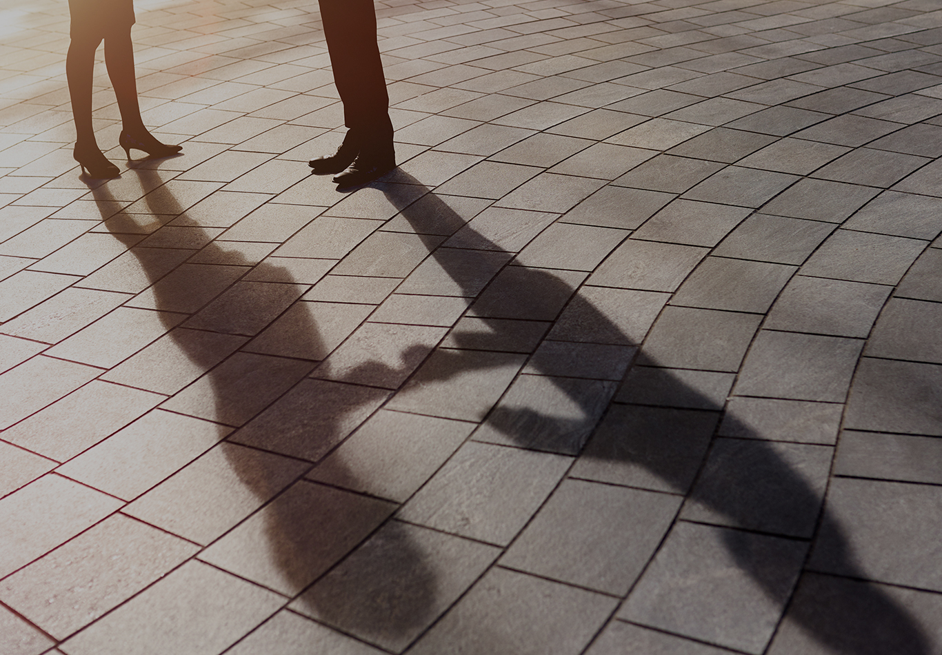 Close up of the legs and feet of a man and woman and their shadows.