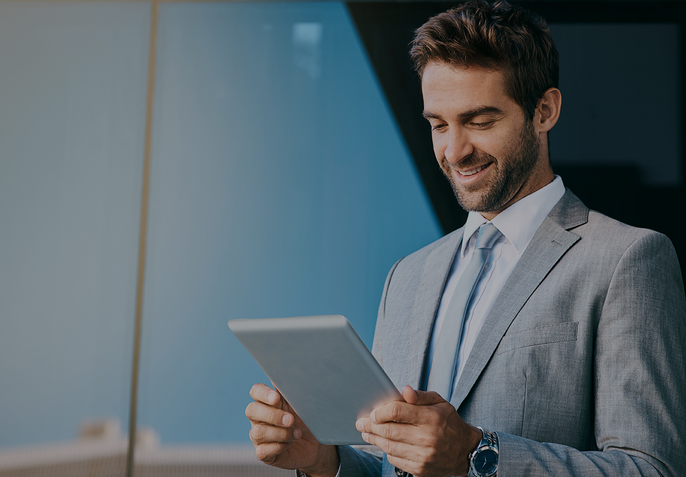 Man in business attire smiling while looking at tablet.