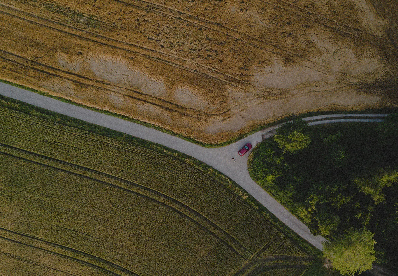 Aerial photo of an empty field with a road through the middle. There is a red car driving down the road. 