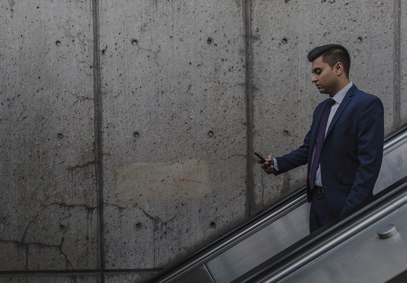 A business man is looking at his phone as they go down an escalator