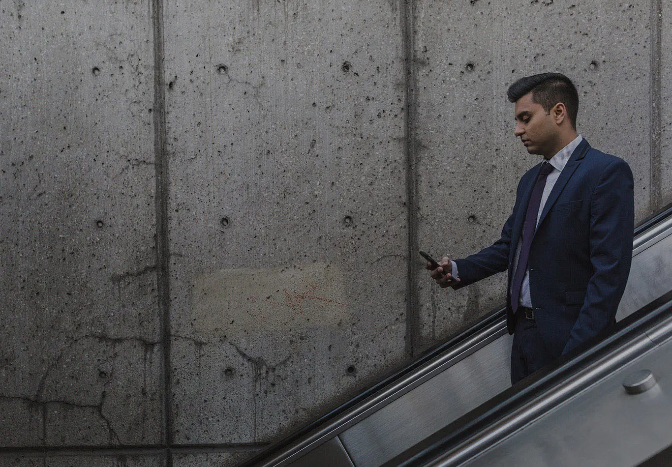 A business man is looking at his phone as they go down an escalator