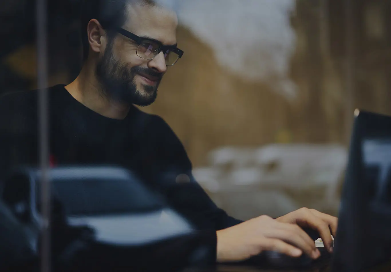 A bearded man wearing glasses is working on a laptop