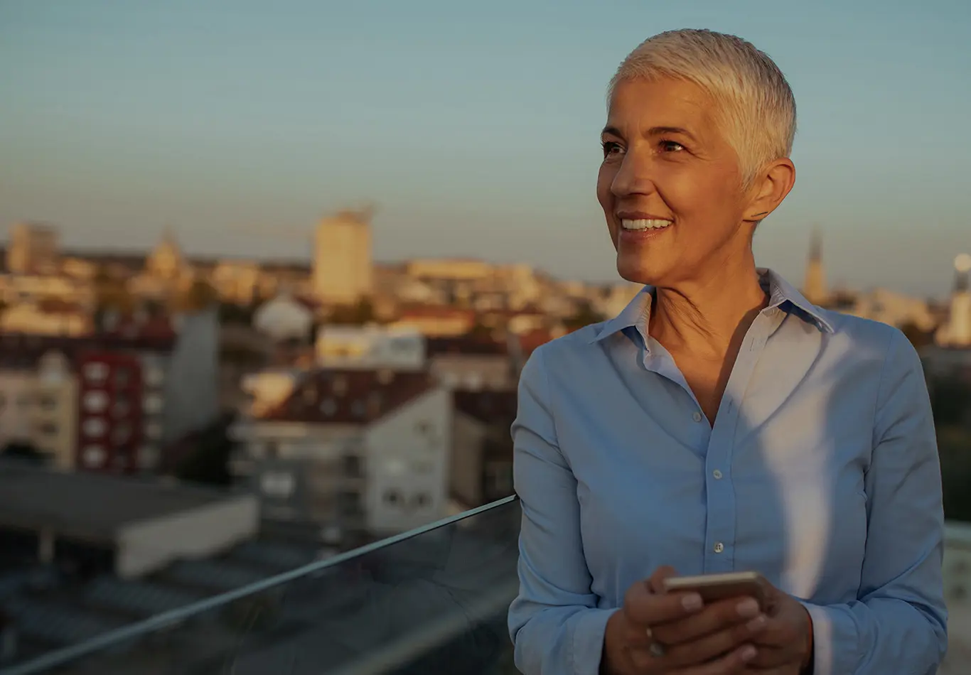 A woman with short hair is holding a phone and looking off into the distance