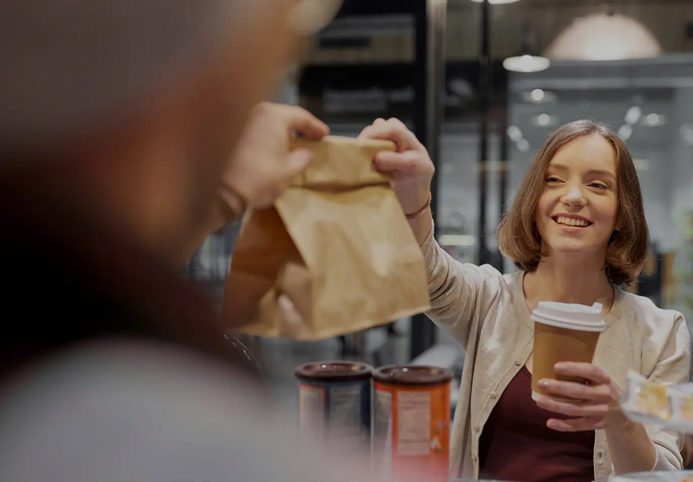 A woman holding a coffee cup is receiving a bag from another person