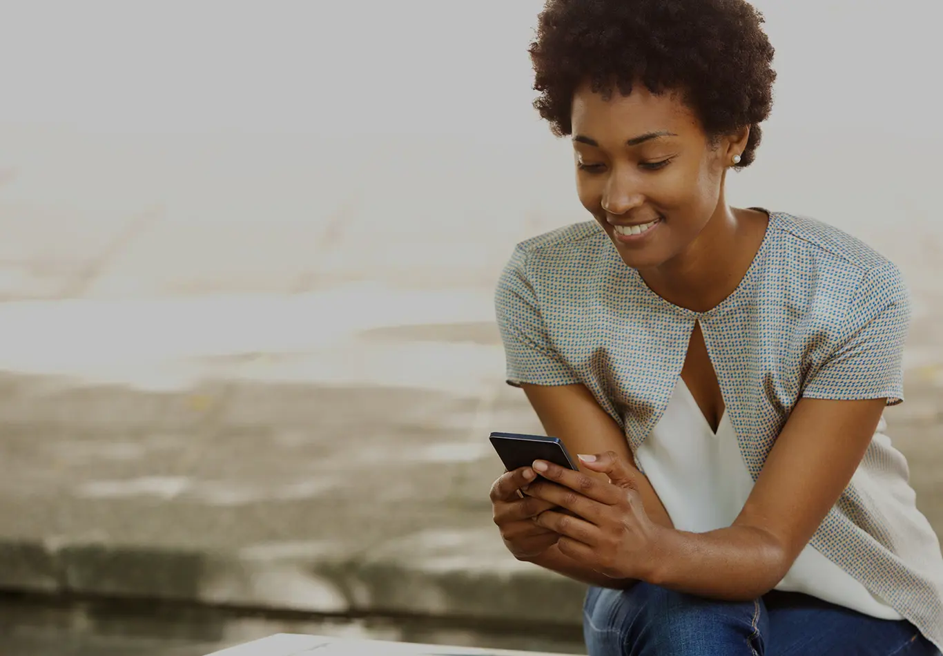 A woman with curly brown hair looks at her phone